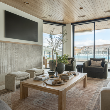 Modern living room with wooden coffee table, armchairs, and large windows overlooking a waterfront.